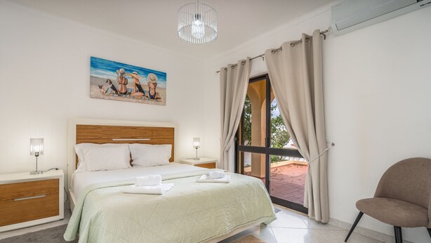 A bedroom with a bed, bedside tables, a chair, a painting, and a window with curtains. - Salicos Benagil Pool Villa (Lagoa)