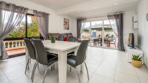 A modern living room with a dining area, large windows with curtains, and a view of the outside. - Salicos Benagil Pool Villa (Lagoa)