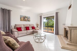 Een woonkamer met een beige bank, rode kussens, een glazen salontafel en een open haard.