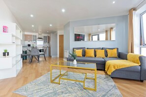Ein modernes Wohnzimmer mit einem grauen Sofa, gelben Kissen und einem Glastisch.