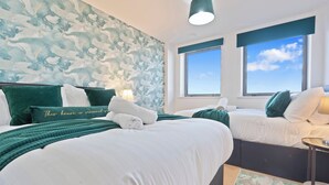 Camera d'albergo con due letti, un'ampia finestra e una parete con un motivo astratto nei toni del blu e del bianco.