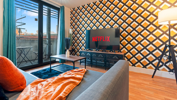 A modern living room with a large flat-screen TV, a sofa, a coffee table, and a patterned wall. - 1 Bed Apartment Sleeps 5 - Balcony - Wifi & Tv (Birmingham)