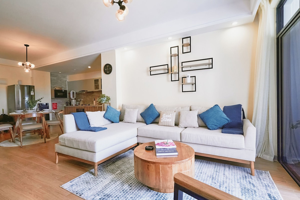 A modern living room with a sectional sofa, a round coffee table, and a dining area with a wooden table and chairs.
