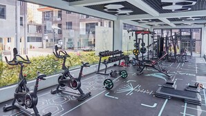 A modern gym with exercise equipment, a patterned floor, and large windows overlooking a residential area.