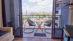 A balcony with a view of the city, two chairs, a small table, and a hanging light fixture.
