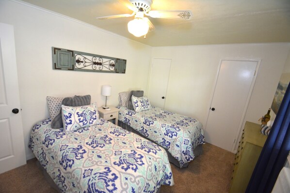 A bedroom with two beds, a ceiling fan, a nightstand, and a decorative wall piece.