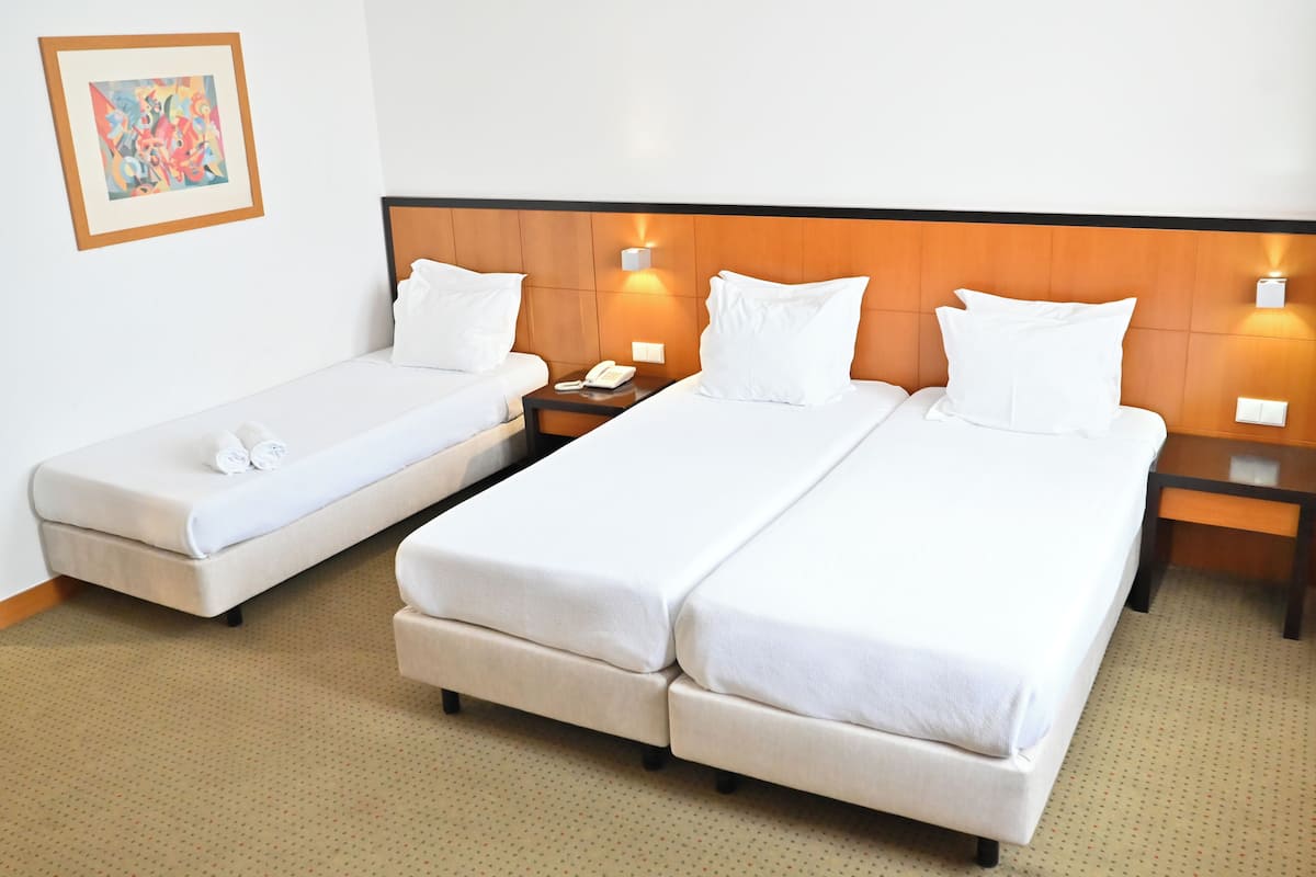A hotel room with two beds, a nightstand with a phone, and a wall-mounted light.