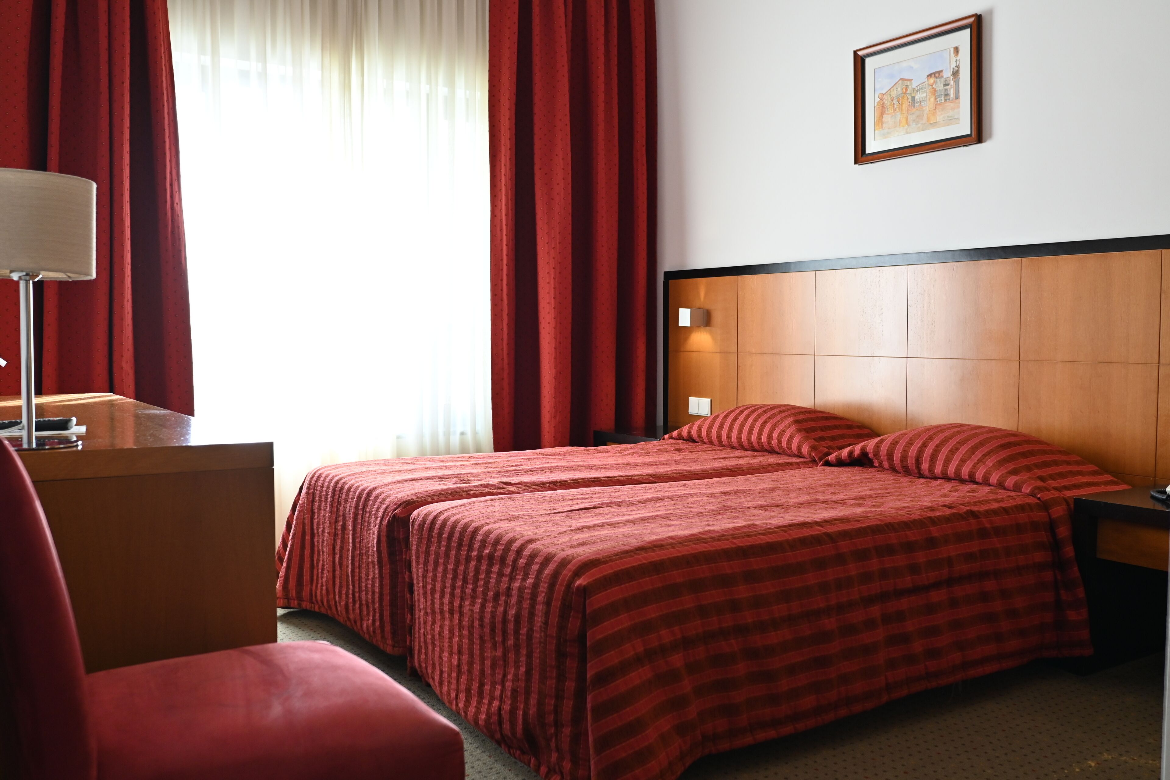 A hotel room with a large bed, a desk, a chair, and a painting on the wall.