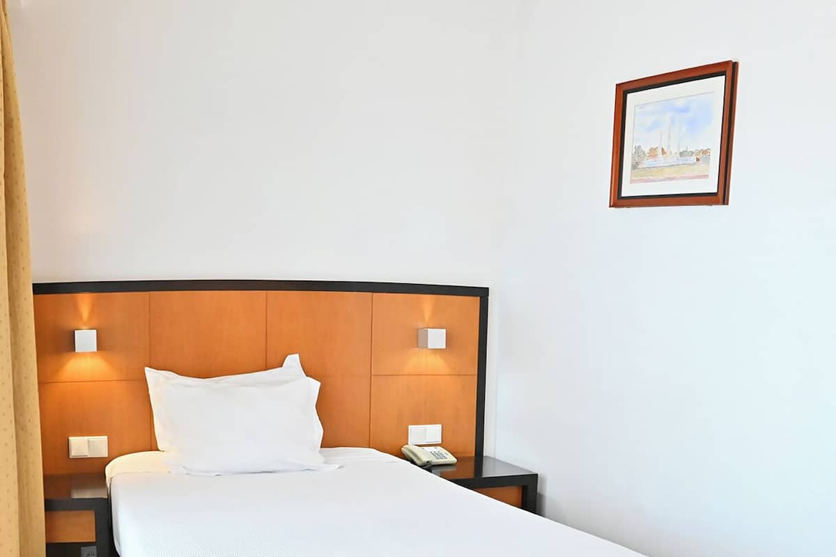 A hotel room with a large bed, two bedside tables with lamps, a telephone, and a framed picture on the wall.