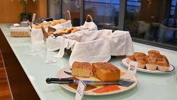 A buffet table with various baked goods, including bread and muffins, and a sign indicating a queue for a specific item.