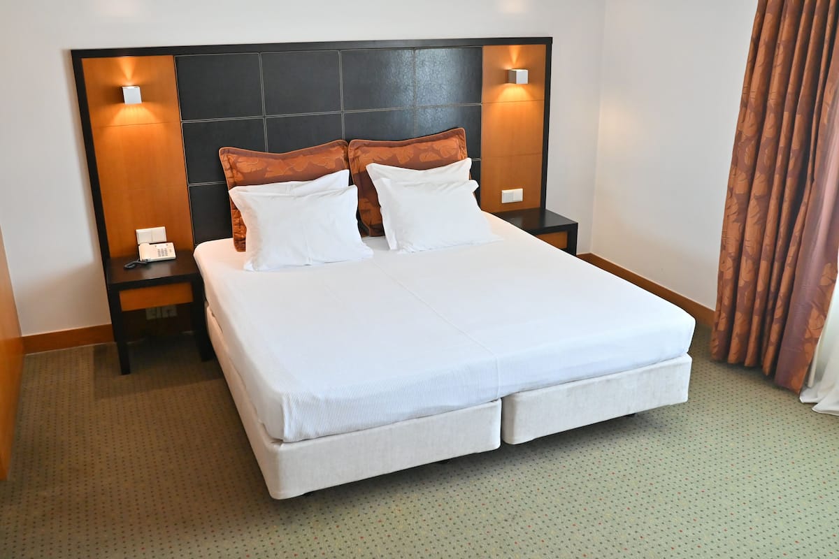 A hotel room with a large bed, two bedside tables with lamps, and a headboard with built-in lighting.