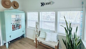 A room with a light blue cabinet, a bench with pillows, and a large plant. There are three windows with blinds, and a sign that says "Lake". - Peaceful water front retreat welcome to Sozo cabin!  (Warsaw)