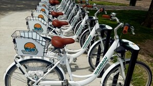 A row of white bicycles with brown seats and baskets, branded 'Warsaw Adventures', parked on a concrete path with a playground and a body of water in the background. - Peaceful water front retreat welcome to Sozo cabin!  (Warsaw)