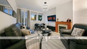 A modern living room with leather sofas, a fireplace, a TV, and a dining area. - Craigievar Crescent Apartment | Grampian Lettings (Aberdeen)
