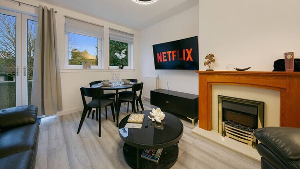 A modern living room with a fireplace, a dining area, and a TV displaying 'NETFLIX'. - Craigievar Crescent Apartment | Grampian Lettings (Aberdeen)