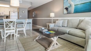 A modern living room with a grey sofa, a coffee table, and a dining area with white chairs and a small table.