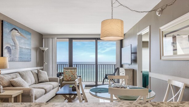 A modern hotel room with a balcony, a large window, a sofa, a dining table, and a painting of a bird.