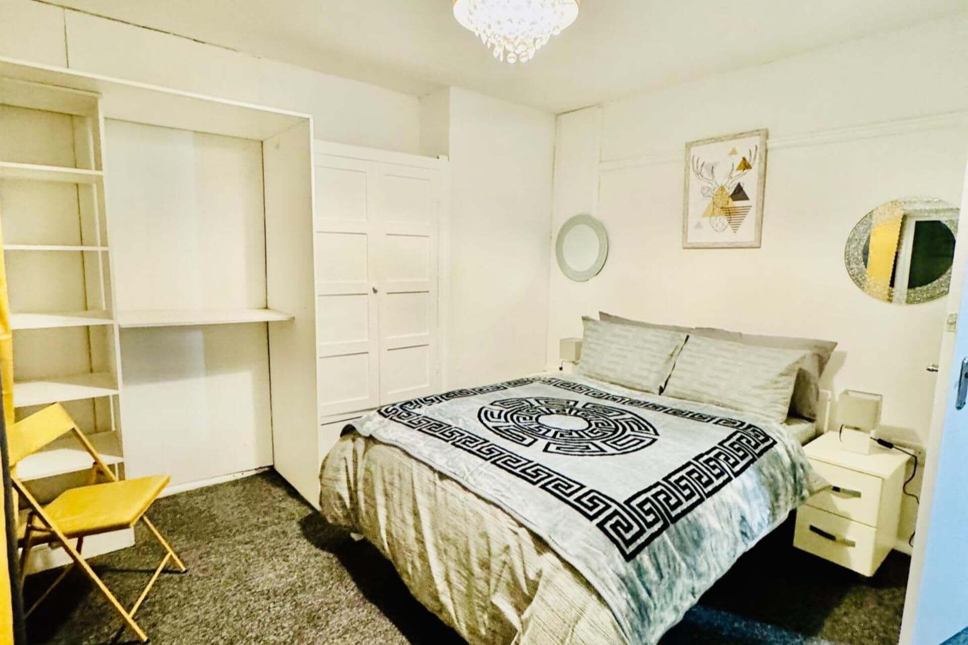 A bedroom with a bed, a wardrobe, a chair, a bedside table, and a mirror.