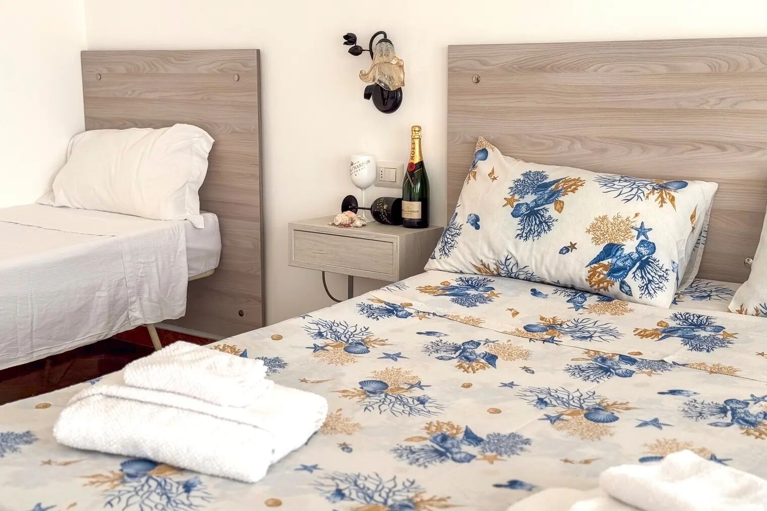 Ein Hotelzimmer mit zwei Einzelbetten, einem Nachttisch mit einer Champagnerflasche und einem Wandbild.
