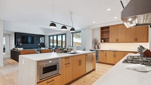 Une cuisine moderne avec des meubles en bois, un grand îlot central, des appareils électroménagers en acier inoxydable et des luminaires suspendus.