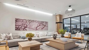 Un salon moderne avec un canapé gris, deux tables basses en bois et une grande fenêtre donnant sur des voitures garées.