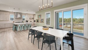 A spacious kitchen with a large island, modern pendant lights, and a view through large sliding doors to an outdoor balcony.