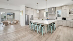 A modern kitchen with a central island, bar stools, and pendant lighting.