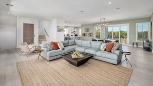 A spacious living room with a light blue sectional sofa, a dark coffee table, and a kitchen in the background.