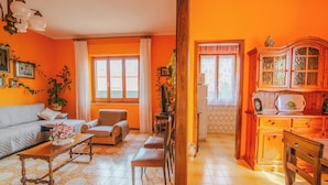 A living room with a sofa, chairs, a coffee table, and a kitchen area with cabinets and a refrigerator. - Villa Corsica (Samatzai)