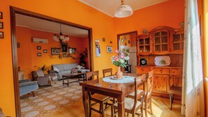A dining area with a wooden table and chairs, a vase with flowers, and a kitchen with wooden cabinets and a refrigerator. - Villa Corsica (Samatzai)