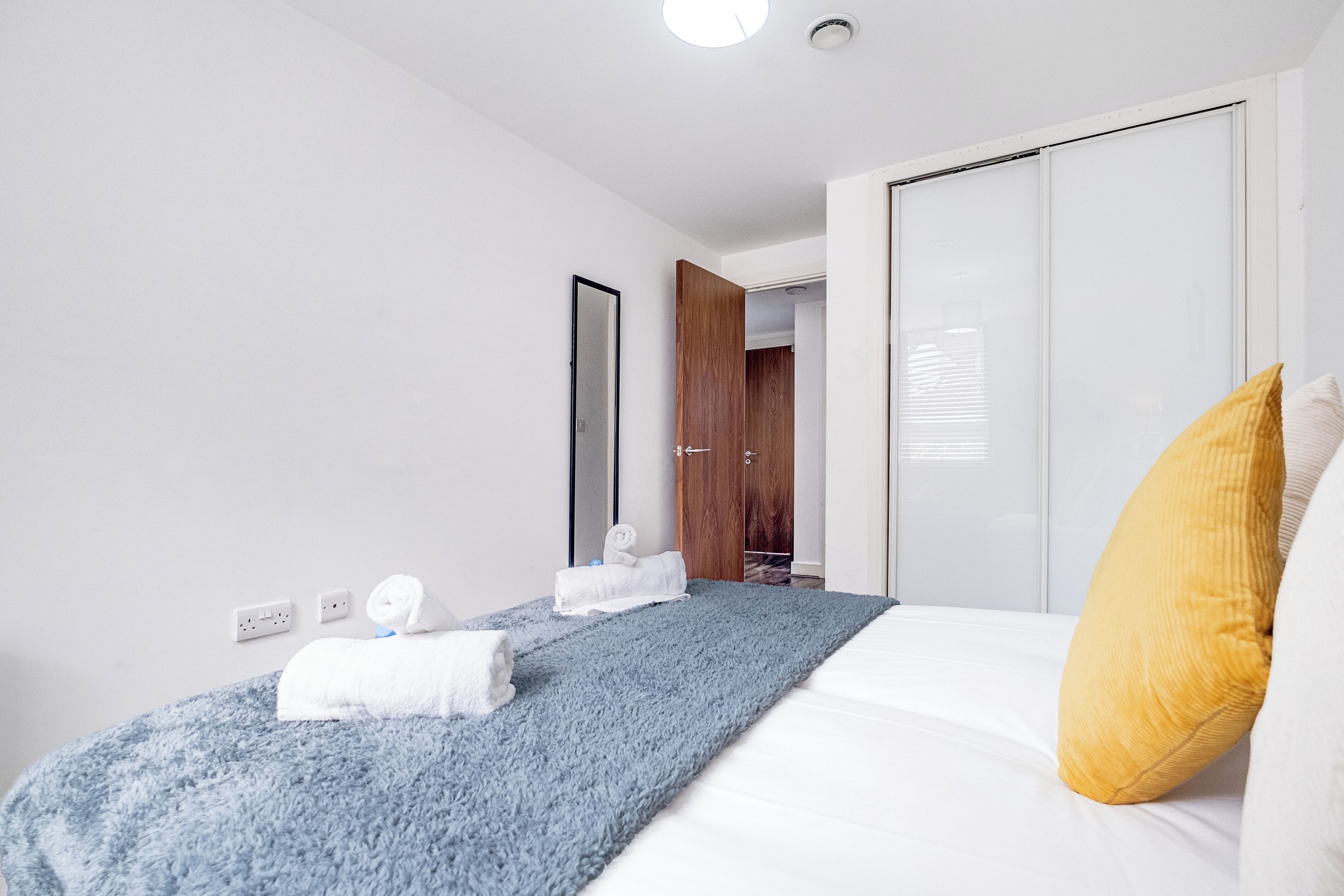 Ein modernes Hotelzimmer mit einem ordentlich bezogenen Bett, einer blauen Tagesdecke und einem gelben Kopfkissen.