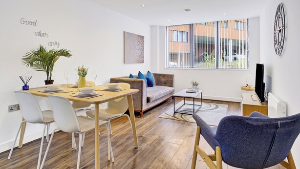 A modern living room with a dining area, a sofa, a coffee table, and a TV. - Cosy Birmingham Apartment - Madison House (Birmingham)