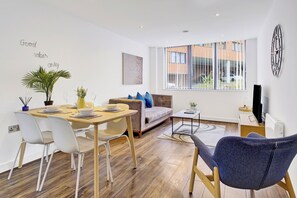 A modern living room with a dining area, a sofa, a coffee table, and a TV. - Cosy Birmingham Apartment - Madison House (Birmingham)