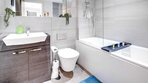 A modern bathroom with a white sink, dark wooden cabinets, a toilet, and a glass-enclosed shower area. - Cosy Birmingham Apartment - Madison House (Birmingham)