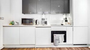 A modern kitchen with white cabinetry, a microwave, toaster, kettle, and a dishwasher. - Cosy Birmingham Apartment - Madison House (Birmingham)