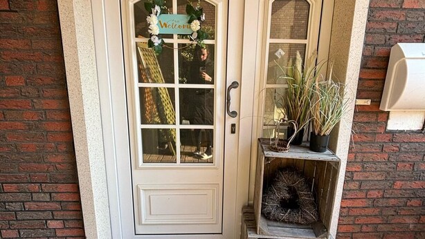 Una puerta blanca con un cartel de 'Welcome', un felpudo y un pequeño estante de madera con plantas.