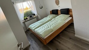 Un dormitorio con cama de madera, ventana con vistas, radiador y decoración en la pared.