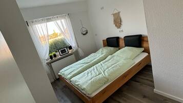 Een slaapkamer met een houten bed, een raam met uitzicht, een radiator en een wanddecoratie.
