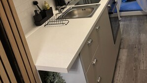 Una cocina moderna con pileta integrada, una mesada pequeña y una ventana con cortinas traslúcidas.
