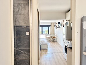Una cocina moderna con lavadora integrada, un comedor con mesa y sillas, y vista al mar a través de un ventanal grande.