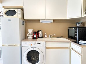 Eine kompakte Küchenzeile mit Mikrowelle, Kaffeemaschine, Toaster, Spüle und Waschmaschine.