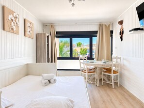 Ein Hotelzimmer mit einem Bett, einem Esstisch mit Stühlen, einem Fenster mit Vorhängen und Kunstwerken an den Wänden.
