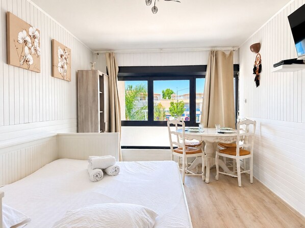 Una habitación de hotel con cama, una mesa de comedor con sillas, ventana con cortinas y obras de arte en las paredes.