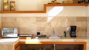 A kitchen with a built-in toaster, coffee maker, and a sink. There are shelves above the counter holding boxes and a fruit bowl. - Casitas with pool & jacuzzi (Todos Santos)