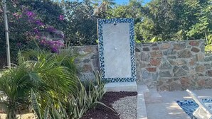 A stone wall with a tiled door, a pool area with lounge chairs, and various plants. - Casitas with pool & jacuzzi (Todos Santos)