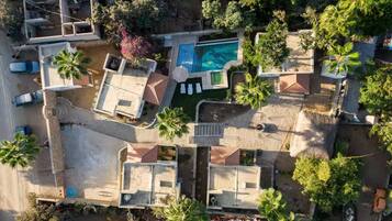 An aerial view of a residential area with a swimming pool, multiple houses, and palm trees.