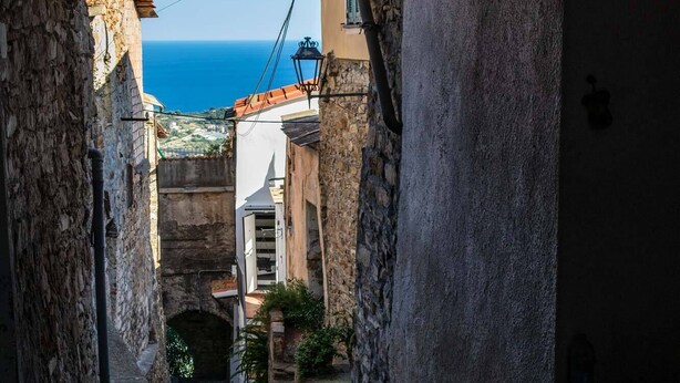 A narrow stone pathway leading through an archway, flanked by rustic stone walls and a view of the sea. - Large panoramic sea view terrace, stone shower, excellence vacation. (Lingueglietta)