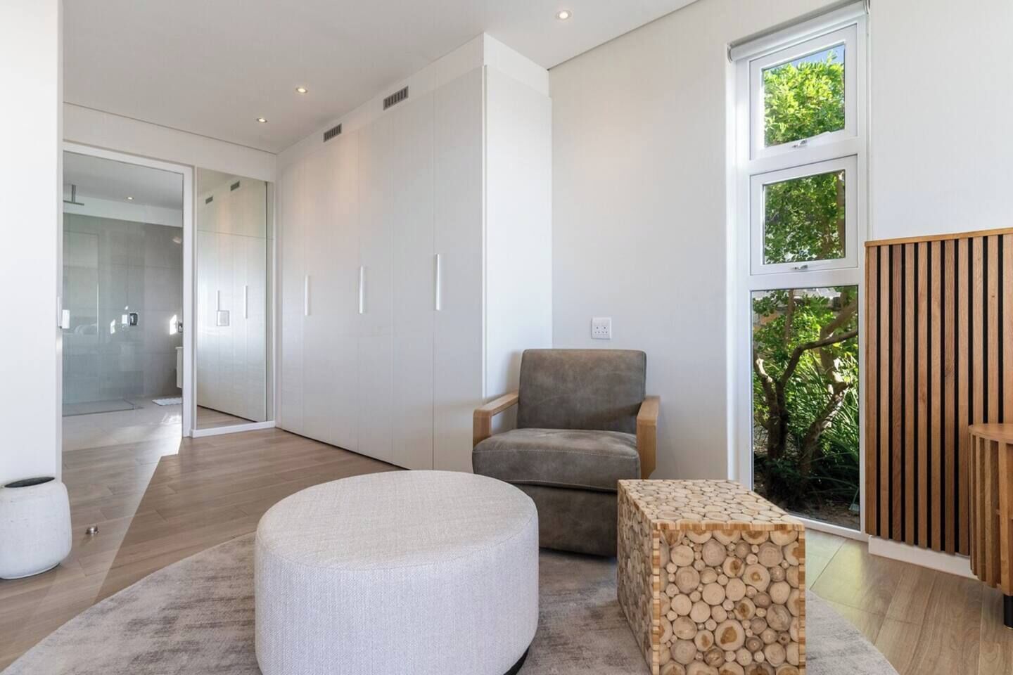 A modern interior with a grey upholstered chair, a round ottoman, and a wooden side table.