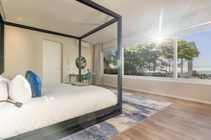 Quarto com cama, escrivaninha, cadeira e vista para o exterior.