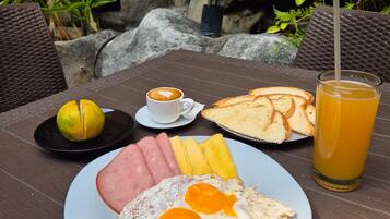 A breakfast plate with ham, eggs, toast, and a glass of orange juice on an outdoor table.